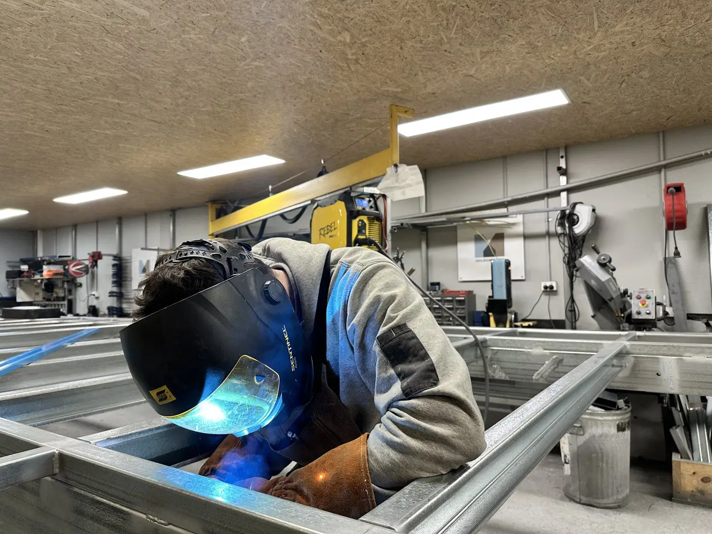 A welder in a helmet and gloves joining the steel framing of a MicroHome in the Melbourne workshop.